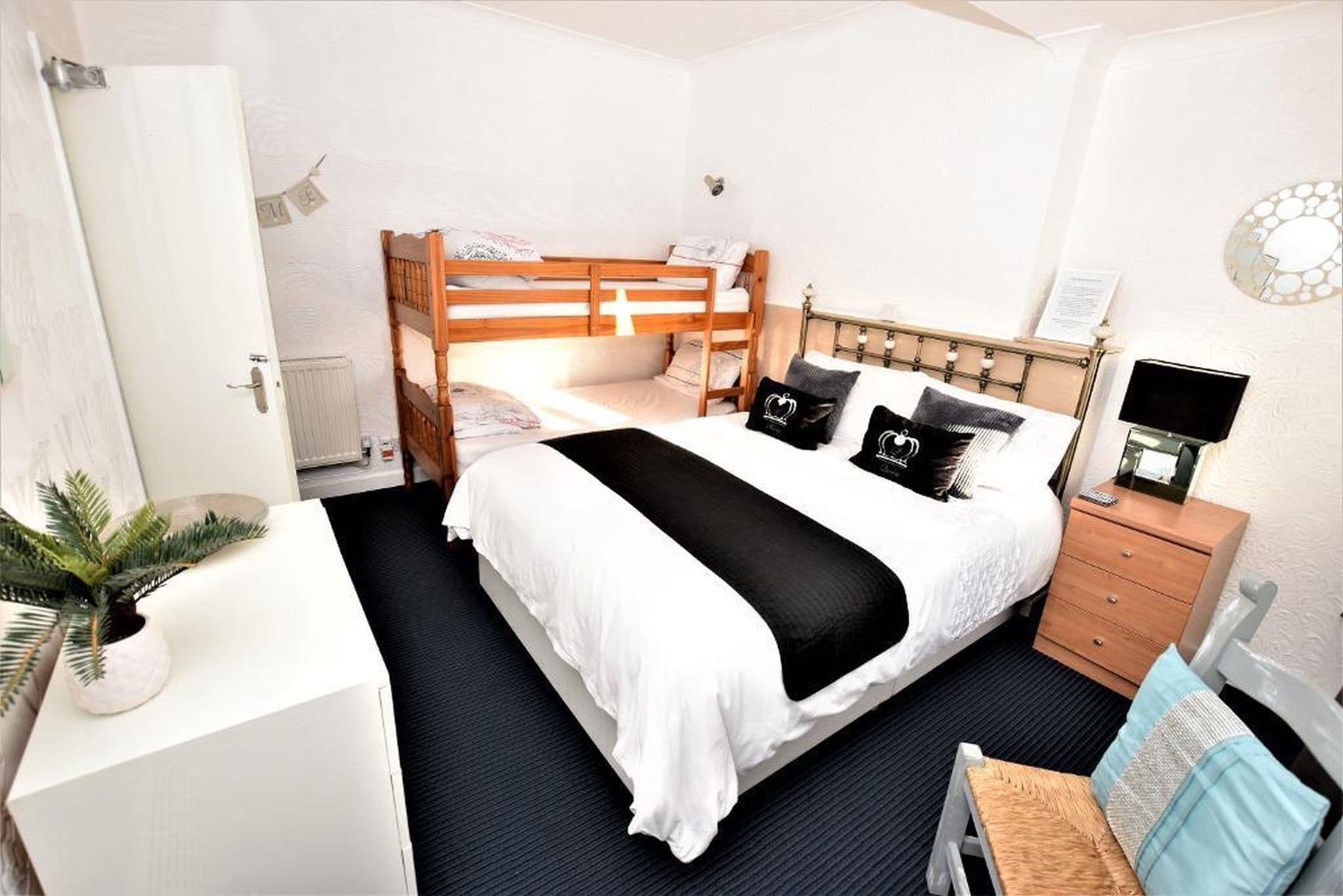 A bedroom with a bunk bed, a bedside table, a chair, a desk, and a potted plant.