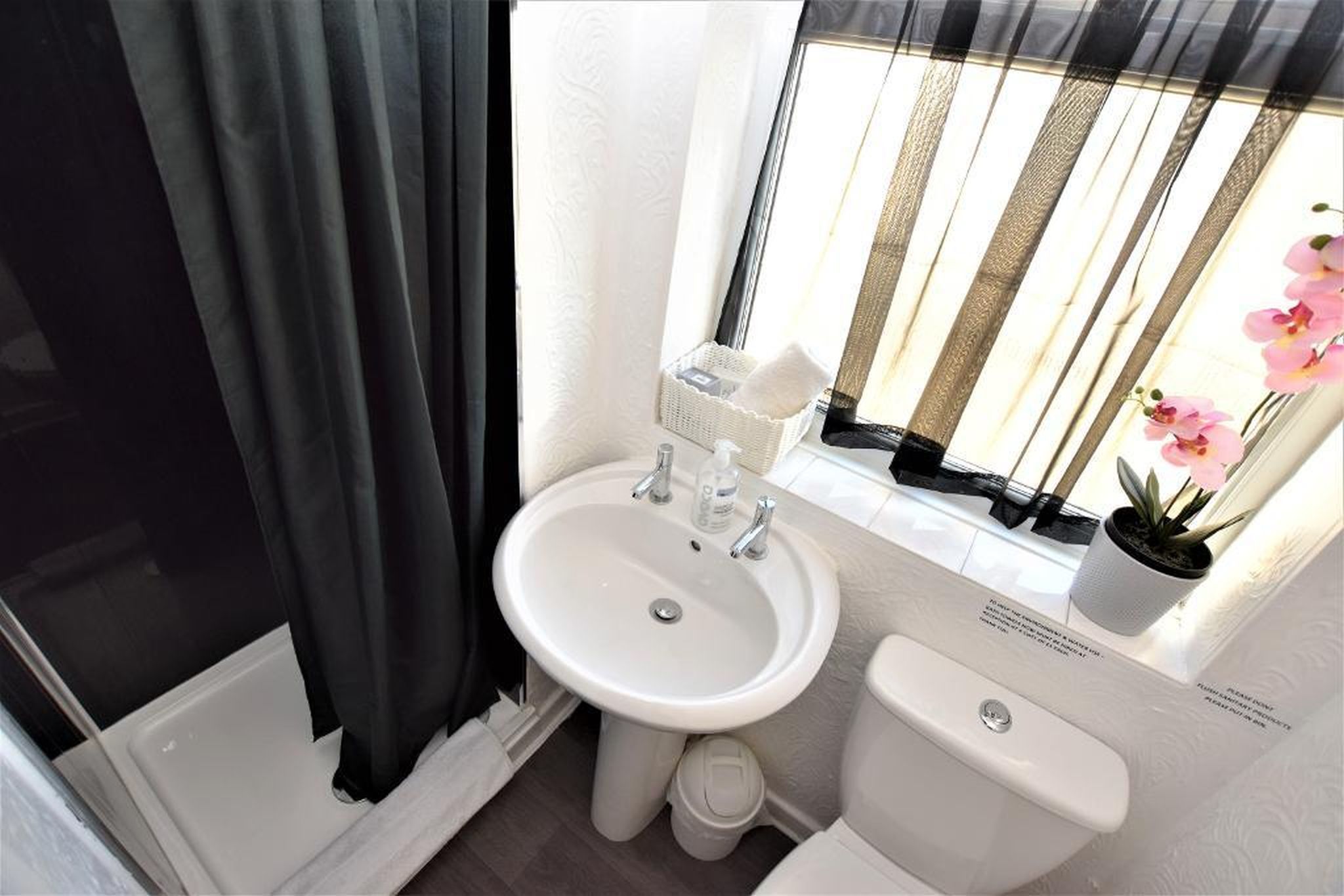 Une petite salle de bain avec un lavabo blanc, des toilettes et une fenêtre avec des rideaux.