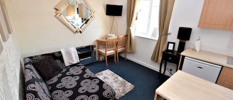 A compact room with a bed, a desk, a chair, a television, and a window with curtains.