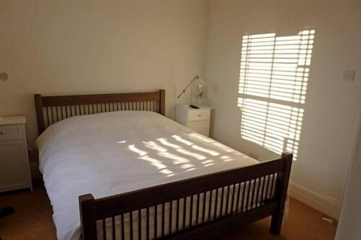 A bedroom with a wooden bed, a nightstand, and a window with blinds.