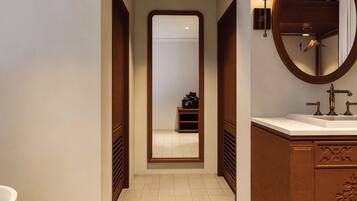 Un pasillo estrecho con un espejo grande, un tocador de madera con un lavabo y un perchero.