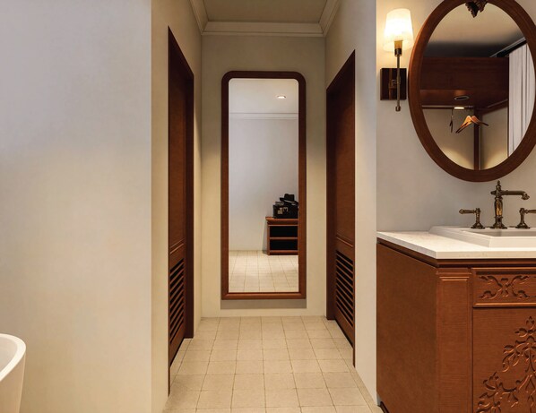 A narrow hallway with a large mirror, a wooden vanity with a sink, and a hanging coat rack.