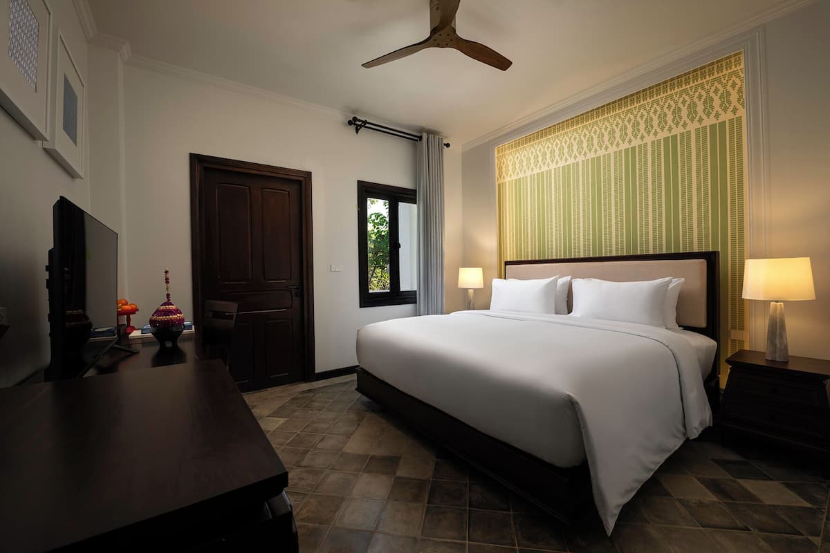 Quarto de hotel com cama, escrivaninha, televisão e janela com cortinas.