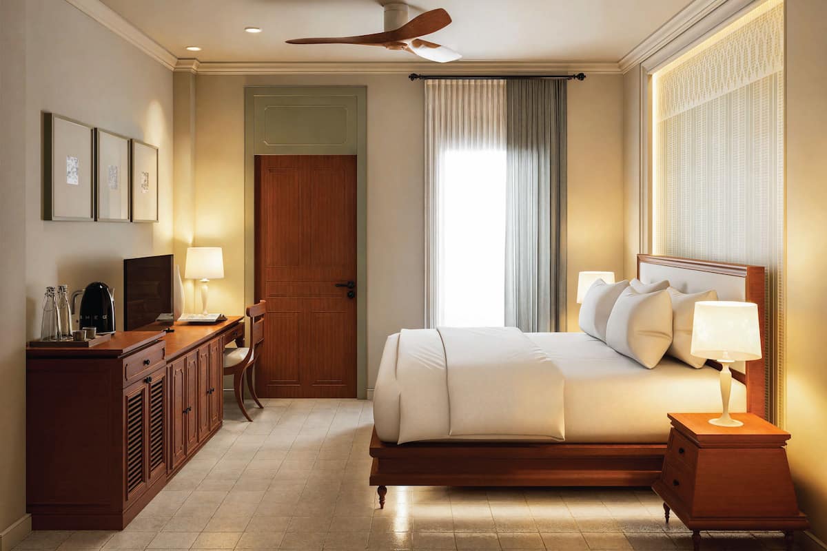 Quarto de hotel com cama, mesa de cabeceira, abajur, escrivaninha com cadeira e ventilador de teto.