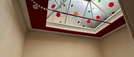 Une pièce avec un plafond rouge, une lucarne ornée de motifs floraux et un lustre.