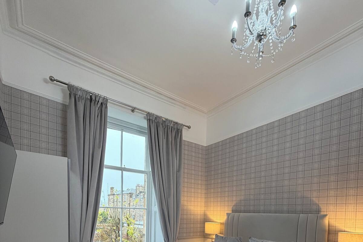 A modern hotel room with a large bed, bedside tables, a desk, and a view of the city.