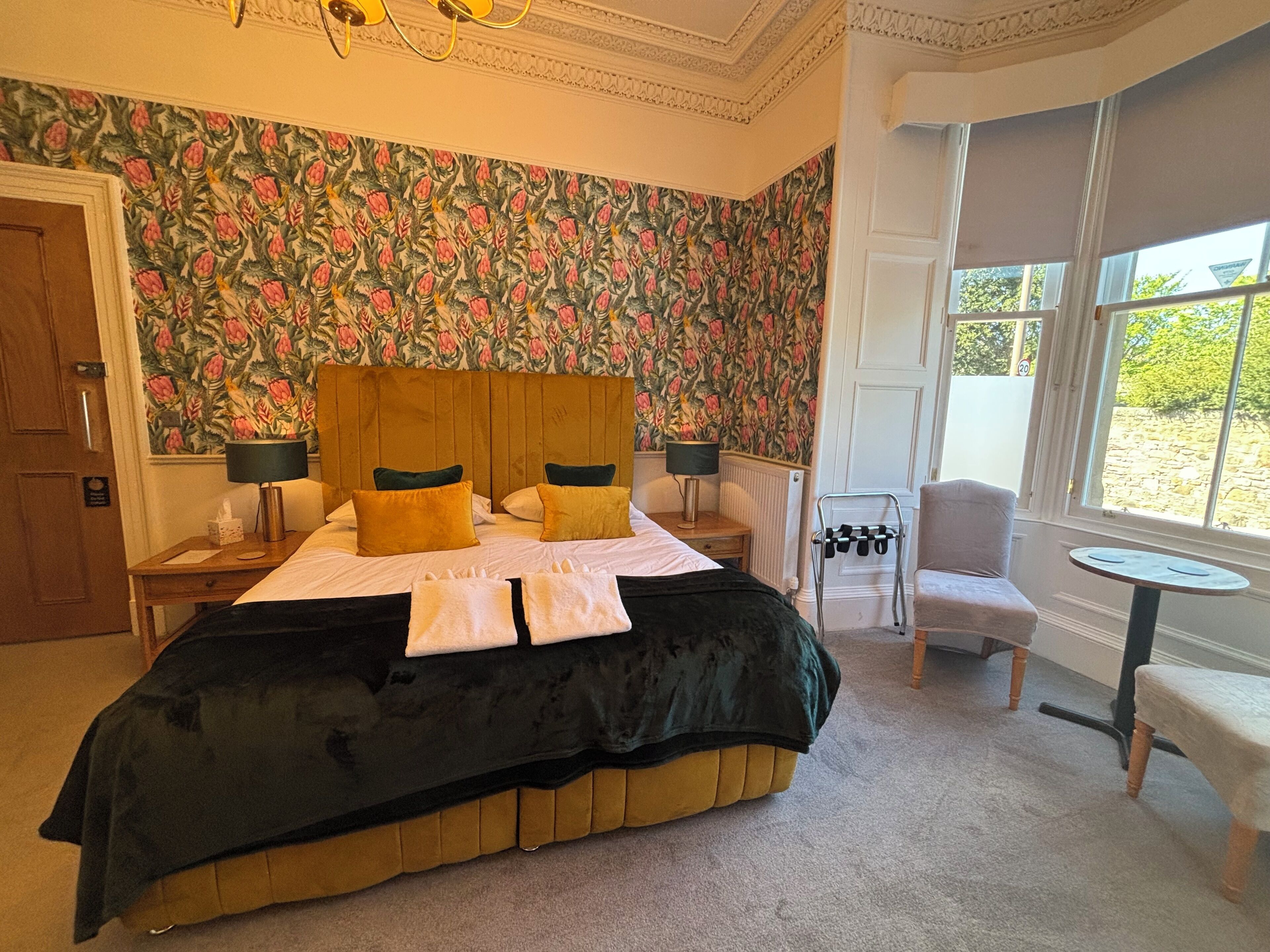 A bedroom with a large bed, two bedside tables with lamps, a chair, and a small table by a window.