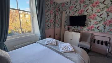 A hotel room with a large bed, a desk with a flat-screen TV, a chair, and a view of the outside.