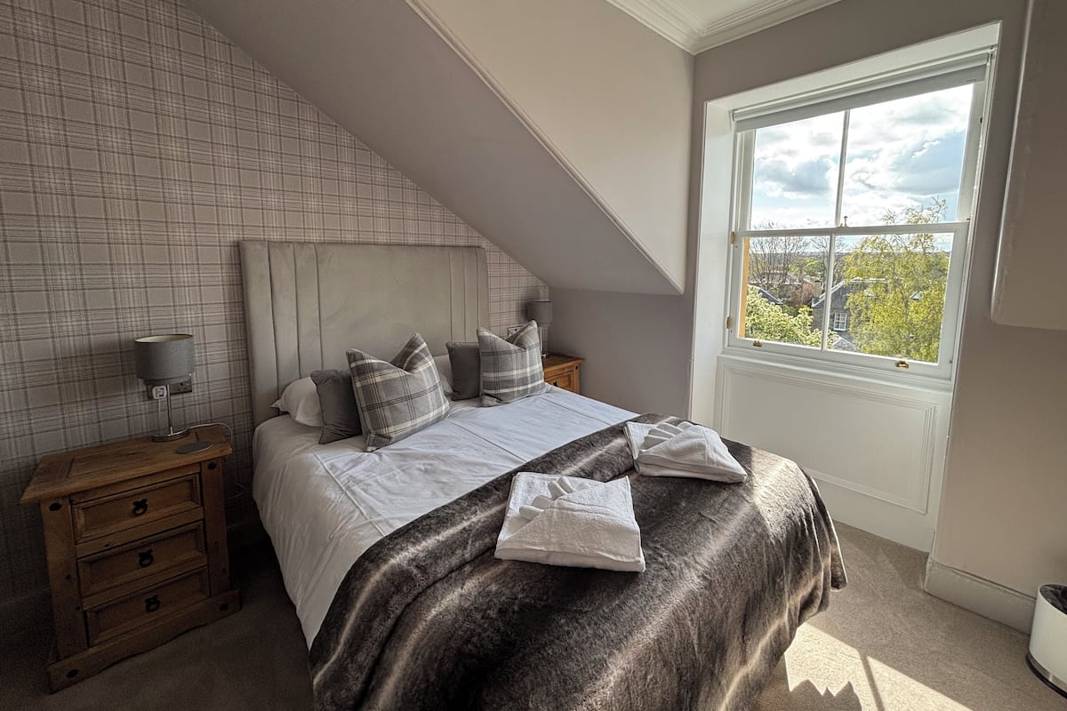 A bedroom with a bed, nightstands, a window, and a view of trees.