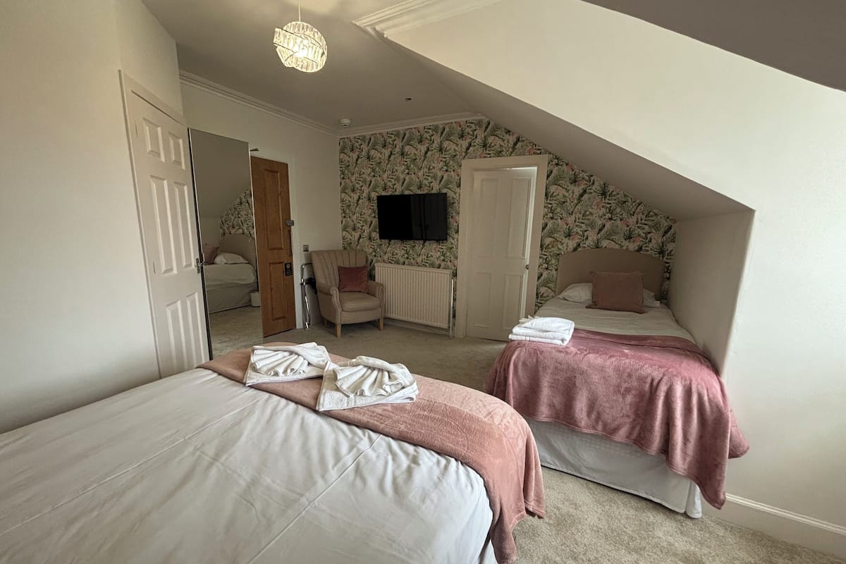 A bedroom with two beds, a radiator, a television, and a chair.