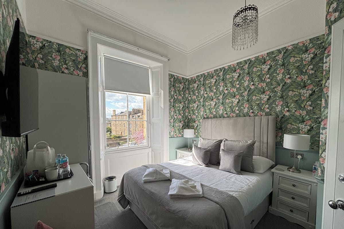 A bedroom with a large bed, a dresser, a vanity, and a window with a view of buildings.