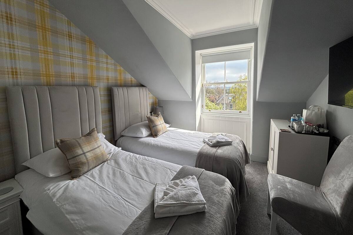 A bedroom with two beds, a window, and a chair.