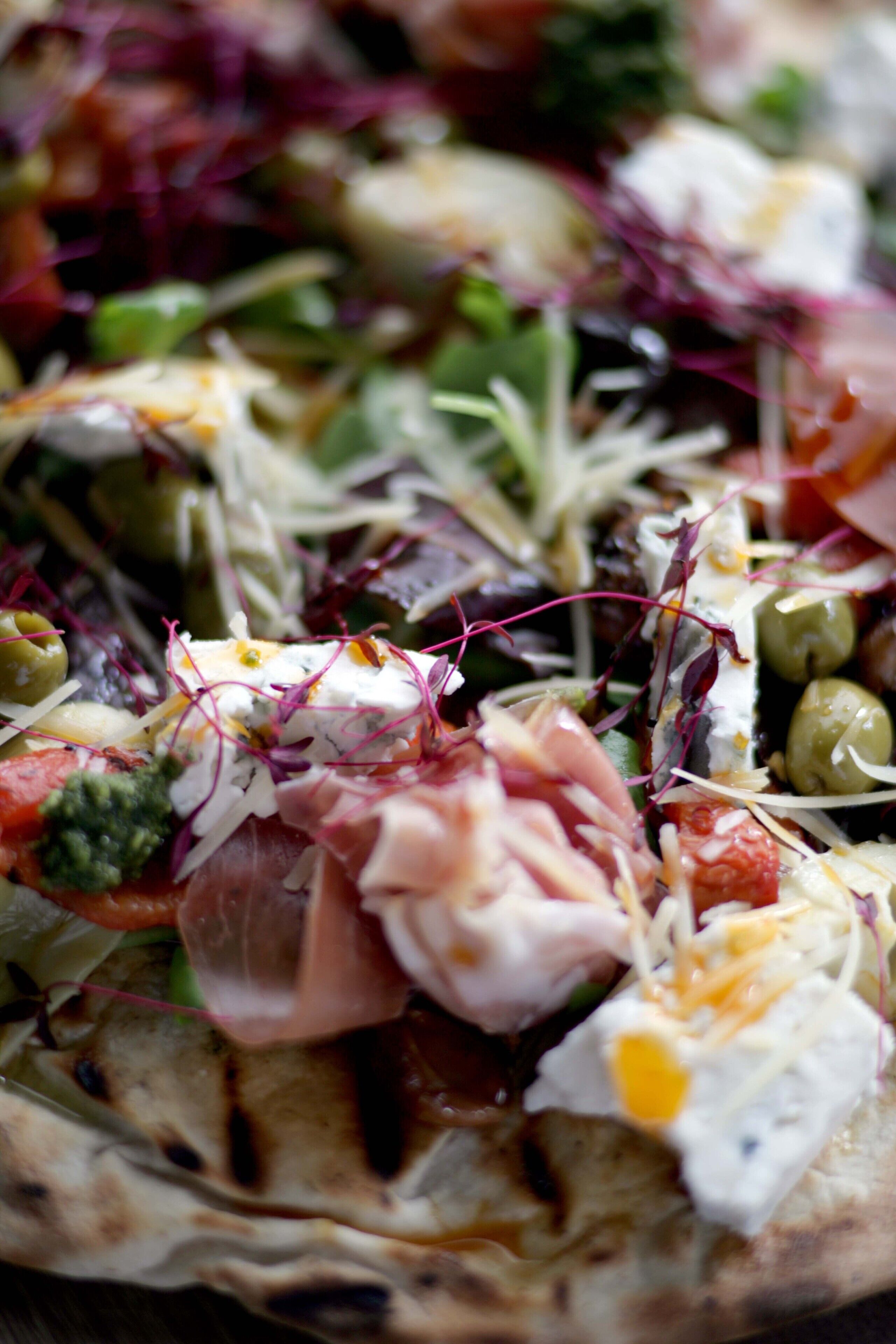 A close-up of a pizza with various toppings including greens, cheese, and meat.