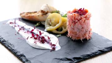 A black slate serving board with salmon, lemon, and a creamy sauce.