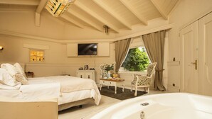 Un dormitorio con una cama grande, una zona de estar con una mesa y sillas, un televisor y una ventana con cortinas.