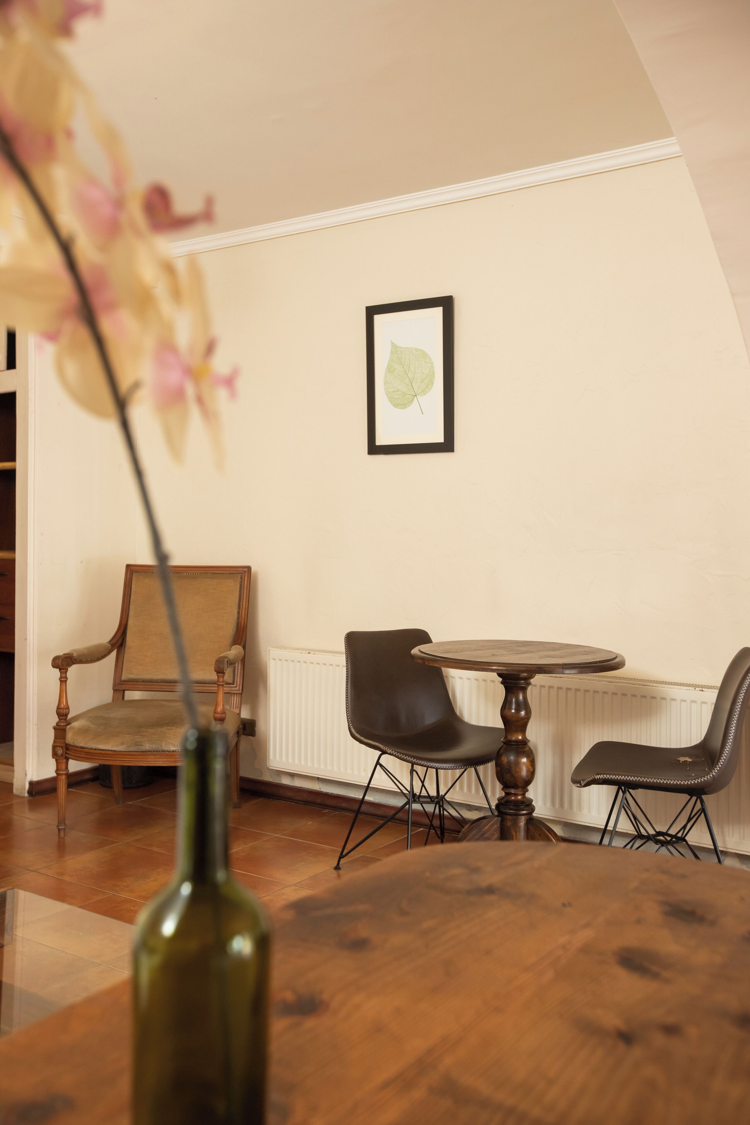 Un comedor con una mesa redonda de madera, dos sillas, un jarrón con flores y un cuadro en la pared.