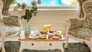 Una habitación con vista a una piscina, una mesa de comedor con alimentos para el desayuno y dos sillones tapizados.
