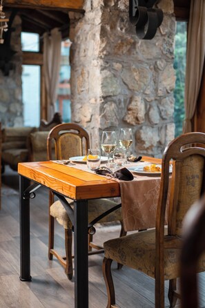 Une table à manger dressée avec des assiettes, des verres et des couverts, dans un intérieur rustique aux murs de pierre et aux meubles en bois.