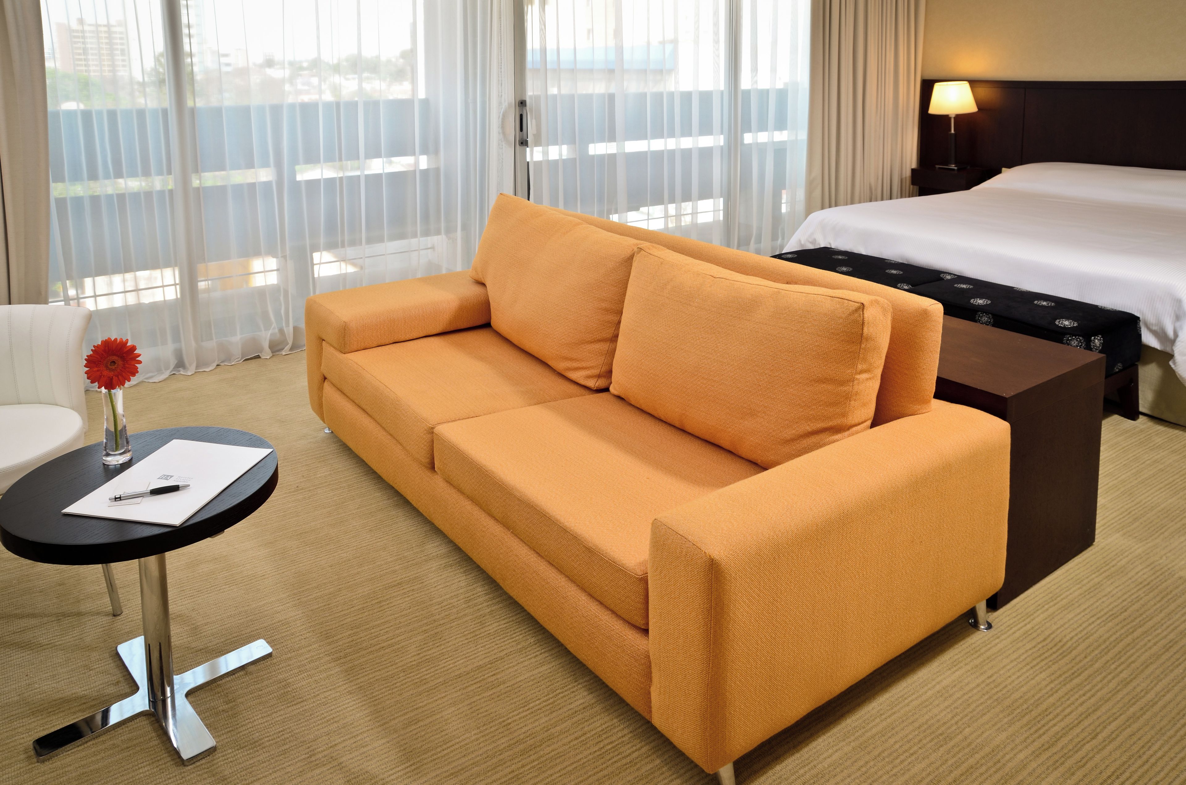 Habitación de hotel con sofá, una pequeña mesa con bolígrafo y papel, lámpara y cama.