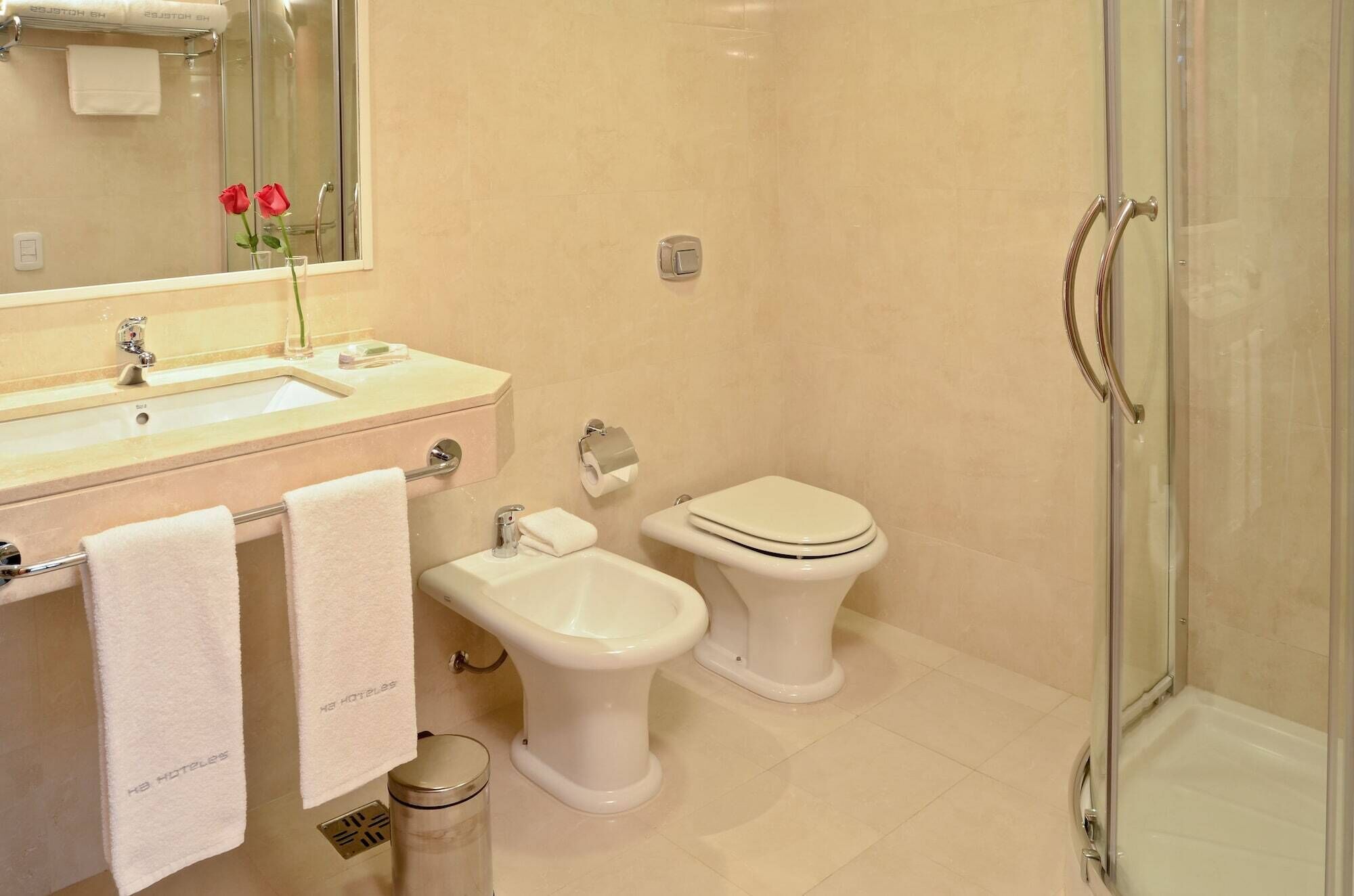 Un baño con lavamanos, bidé, inodoro y ducha con mampara de vidrio.