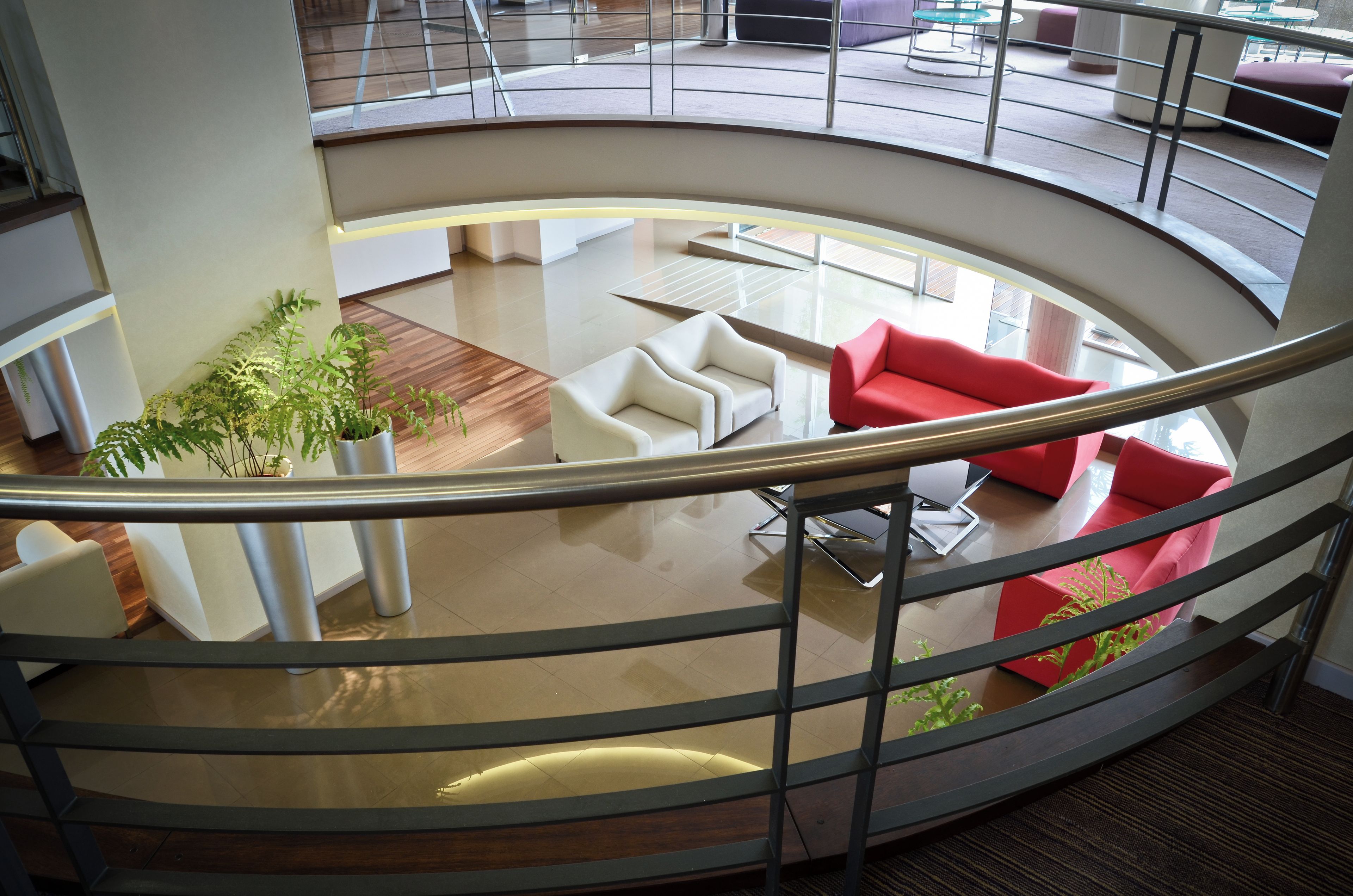 A modern interior with a curved staircase, a seating area with white and red sofas, and a potted plant.