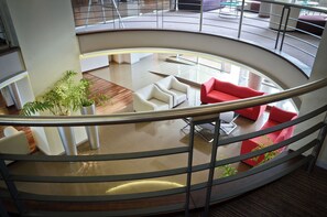 A modern interior with a curved staircase, a seating area with white and red sofas, and a potted plant.