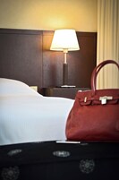 Una habitación de hotel con una cama, una mesita de noche, una lámpara y un bolso.