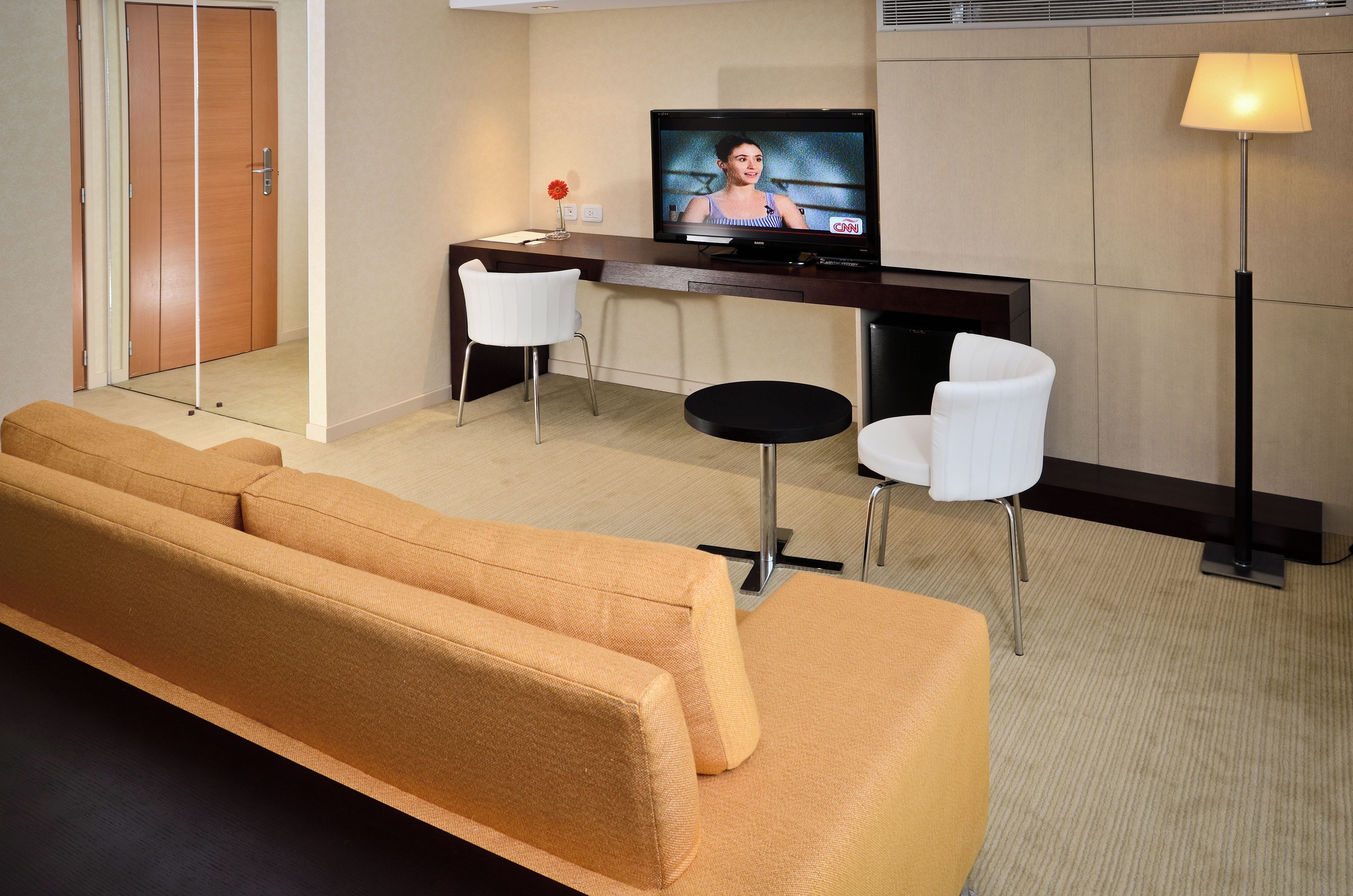 A hotel room with a sofa, two chairs, a small table, a television, and a lamp.