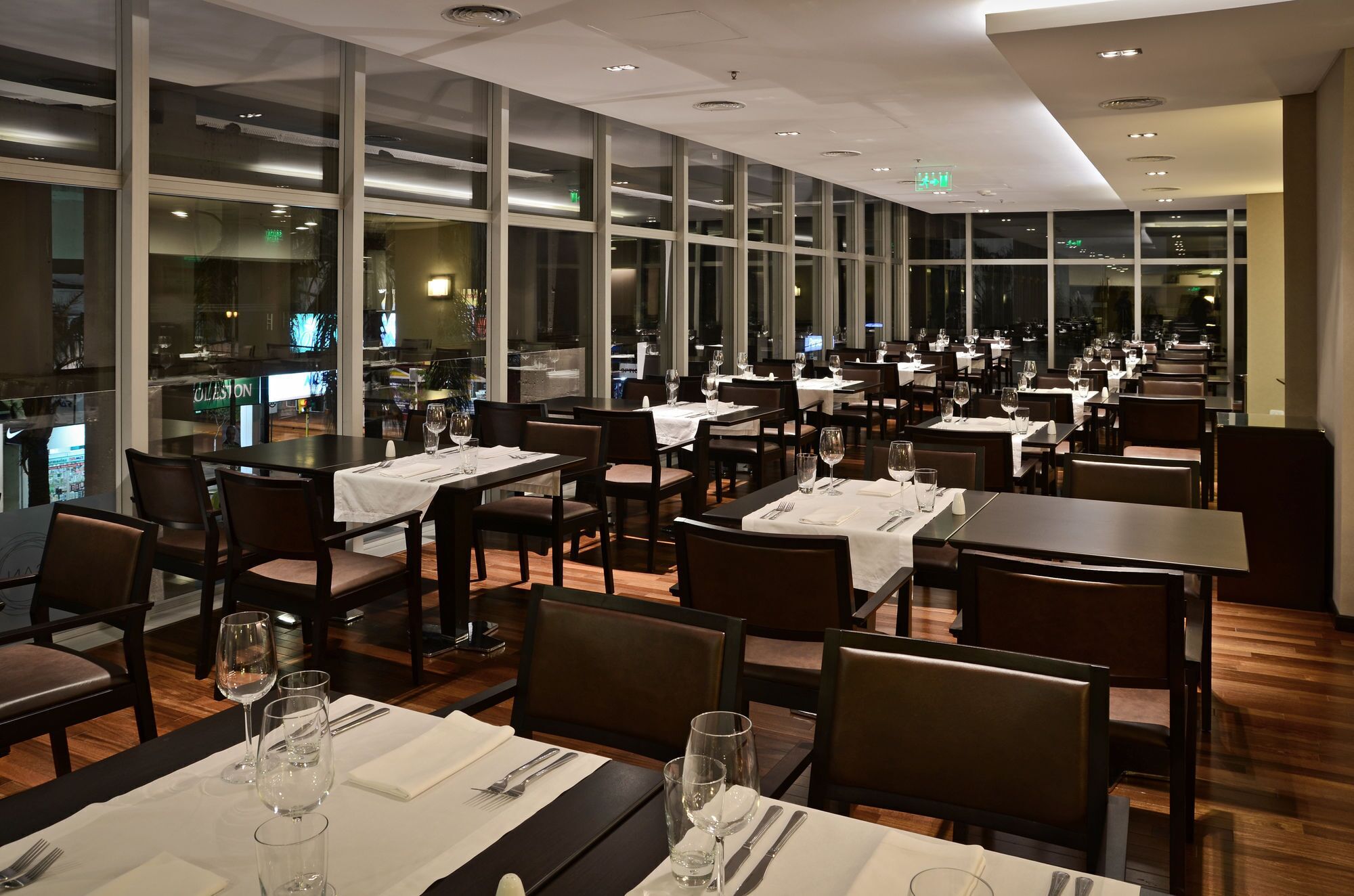 A restaurant with multiple tables and chairs, large windows, and a modern ceiling design.