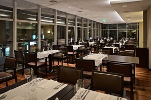 A restaurant with multiple tables and chairs, large windows, and a modern ceiling design.