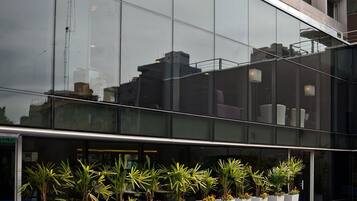 A modern building with a reflective glass facade, a swimming pool with a metal ladder, and potted plants arranged in a row.