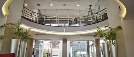 A spacious atrium with a glass railing, a mezzanine level, and potted plants.