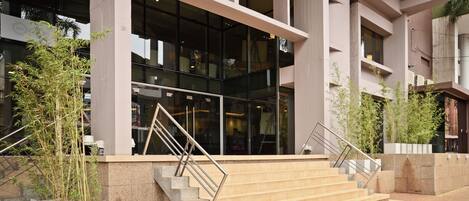 A modern building with a glass facade, concrete columns, and a set of outdoor stairs leading to the entrance.