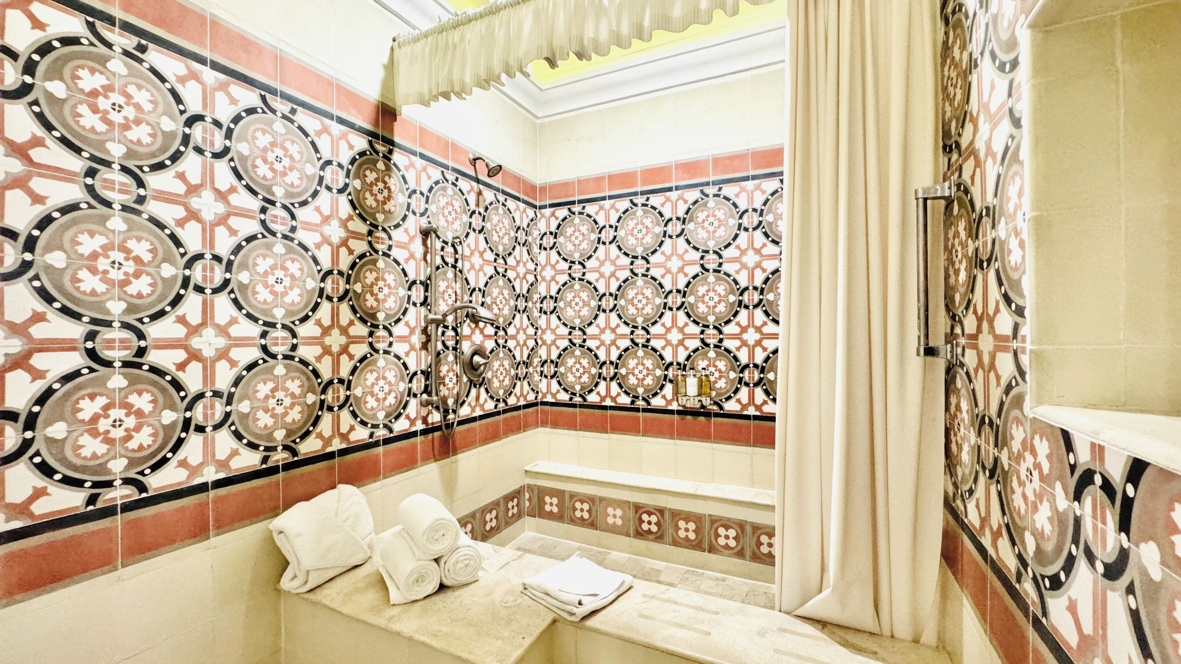 A bathroom with patterned tiles, a bathtub, and towels.