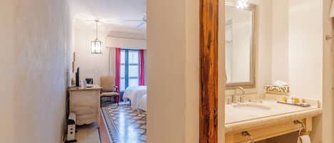 A hotel room with a bed, a desk, a chair, a large mirror, and a bathroom with a sink and towel rack.