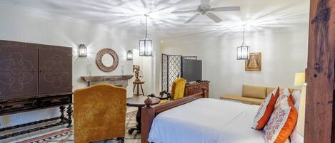 Habitación de hotel con una cama grande, un escritorio de madera, un televisor y una zona de estar con sofá y sillones.