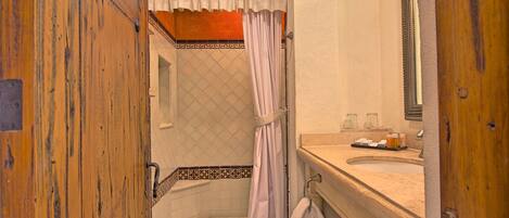 Une salle de bain avec une porte en bois, une douche avec un rideau, un lavabo avec des articles de toilette et un miroir.