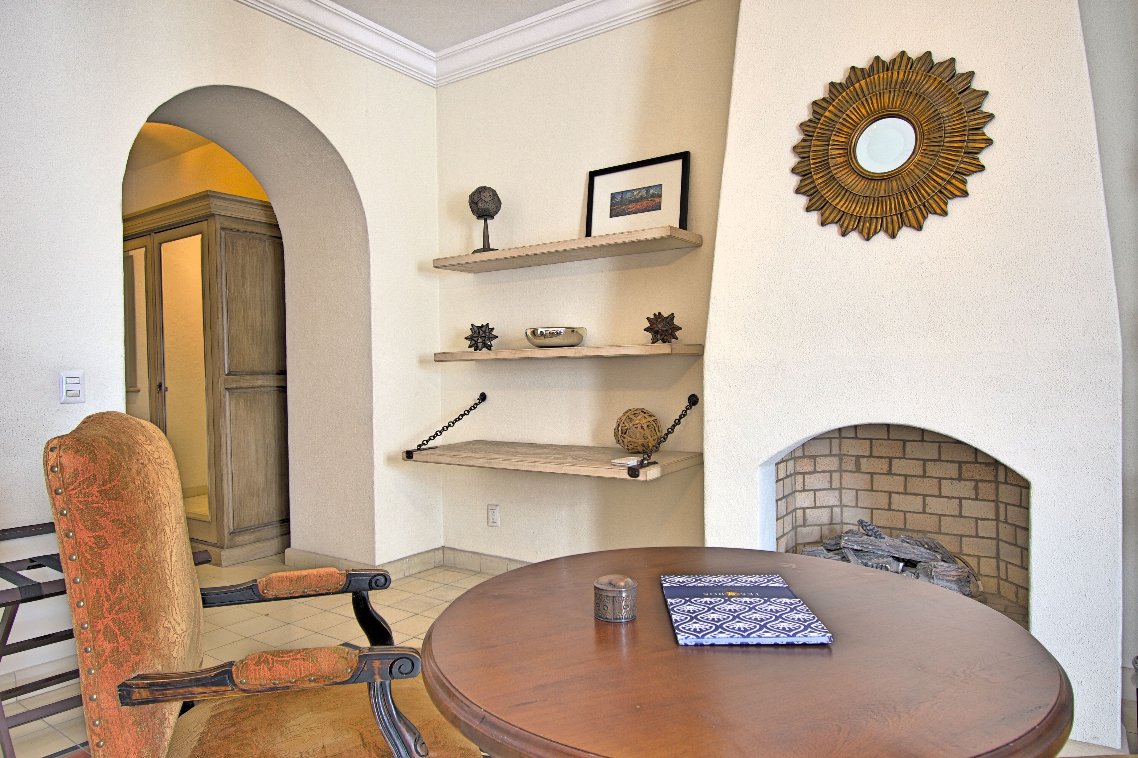 A dining area with a round wooden table, a chair with a leather seat, and a fireplace with a brick surround.