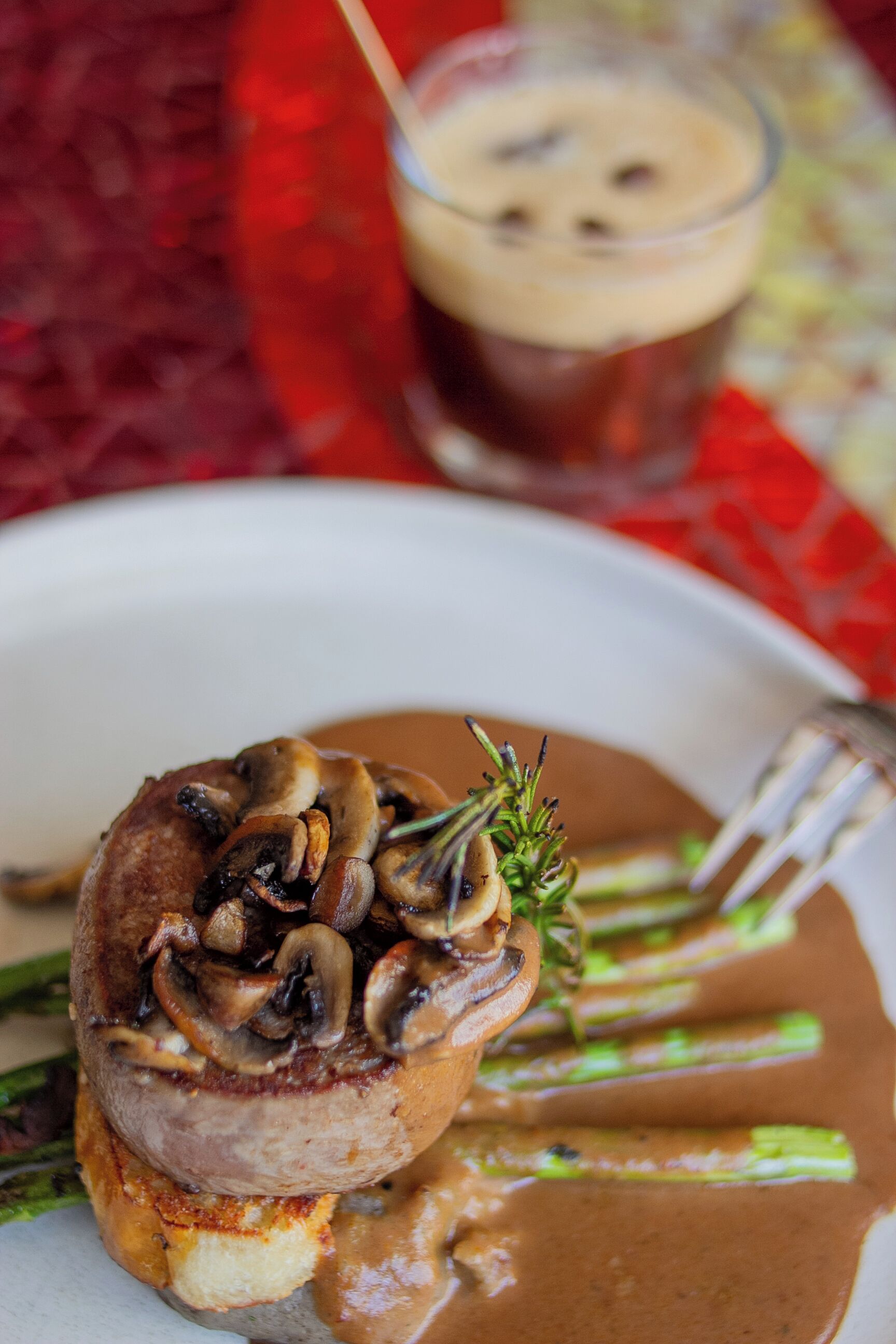 A plated dish with a mushroom-topped meat, asparagus, and gravy.