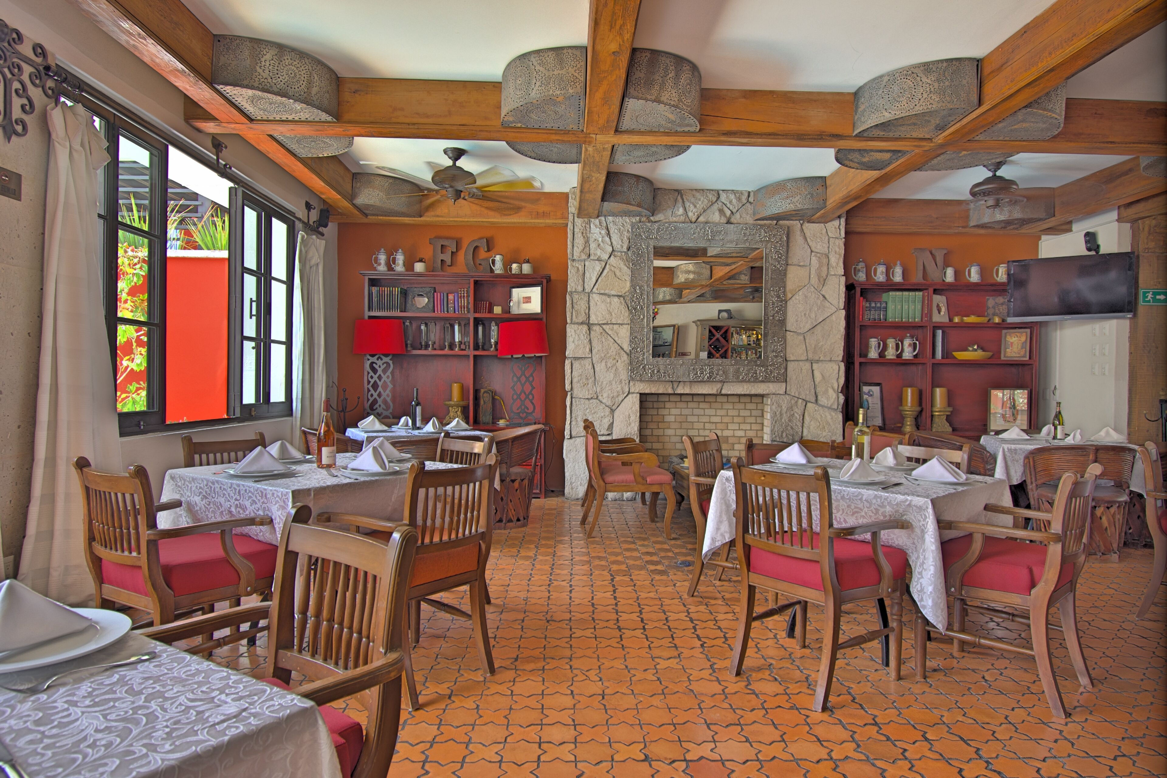 Un restaurante con mesas y sillas de madera, una chimenea de piedra y estanterías con libros y objetos decorativos.