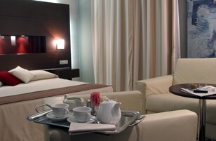 A hotel room with a bed, a sofa, a small table with a tray of breakfast items, and a painting on the wall.