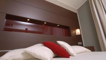 A hotel room with a large bed, a headboard with integrated lighting, and a view of the room's interior through a window with curtains.