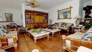 Ein Wohnzimmer mit Fliesenboden, Holzmöbeln, einem Deckenventilator und einem Bücherregal.