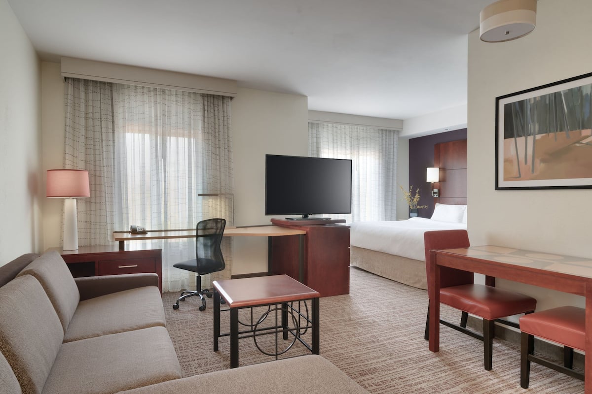 A hotel room with a bed, a desk, a television, a sofa, and a chair.
