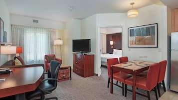 Una camera d'albergo con zona pranzo, televisione, letto e un quadro appeso al muro.