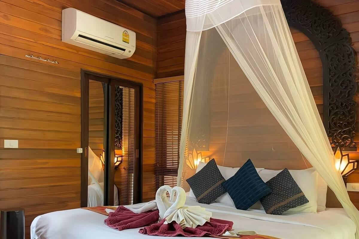 Een kamer met houten lambrisering, een bed, een airconditioning en decoratieve kussens.