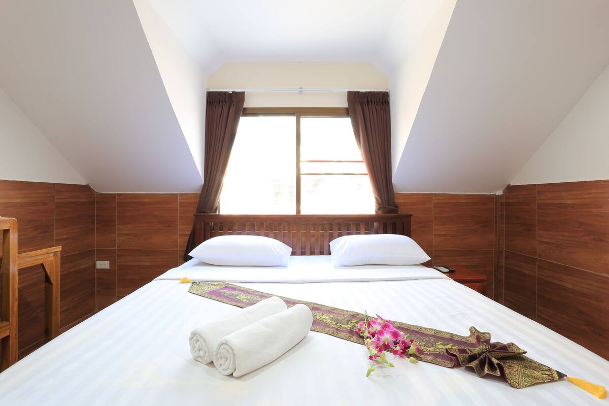 A hotel room with a large bed, wooden headboard, and a window with curtains.