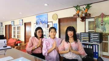 Three guests stand behind a reception desk with a clock on the wall and a shelf holding a framed picture and a Buddha statue.