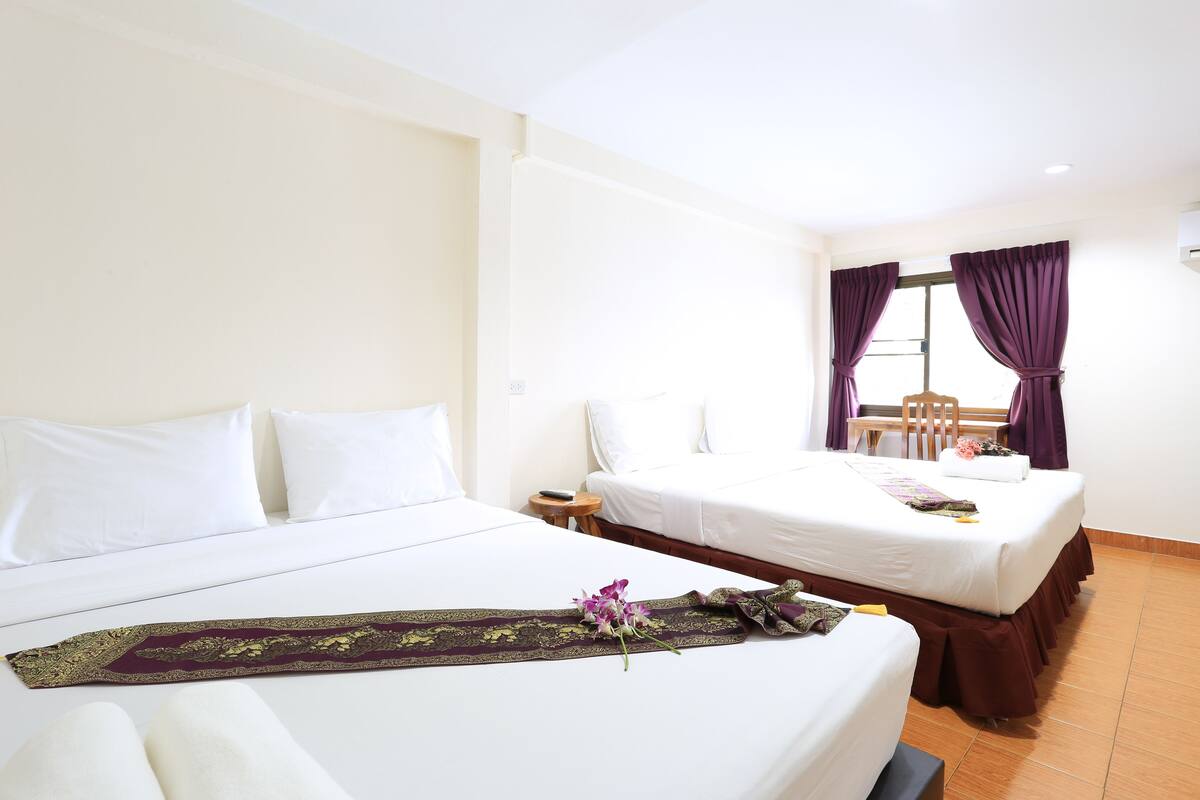 A hotel room with two beds, a nightstand, a chair, and a window with purple curtains.