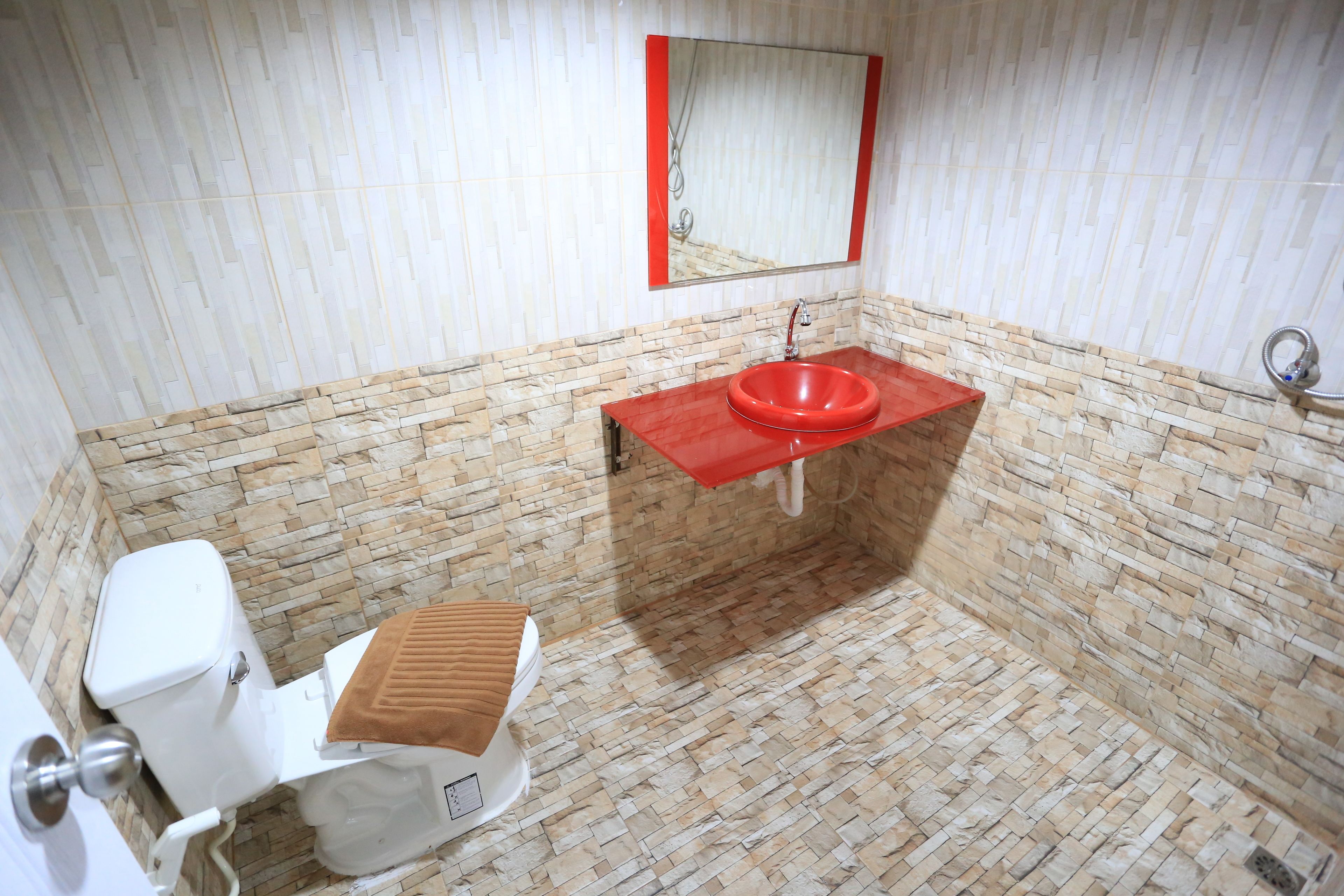 A bathroom with a white toilet, a red sink, and a mirror above the sink.